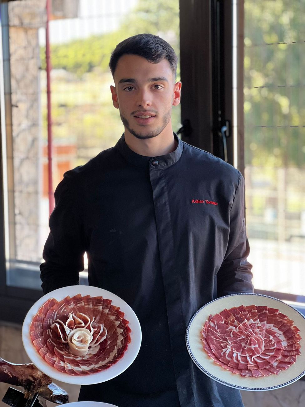 Adrián Torrente, cortador de jamón profesional, con dos platos de jamón ibérico emplatados en rosa